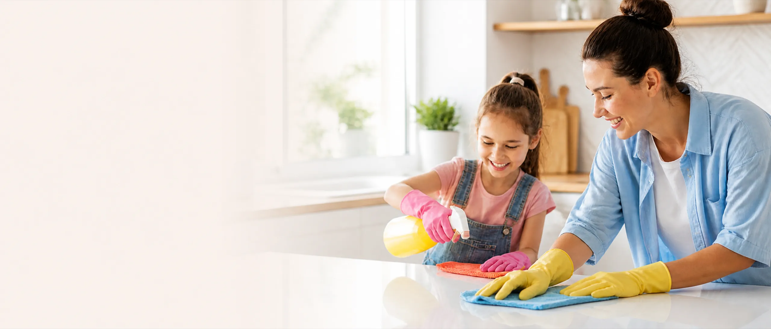 A mother and daughter wiping down a bright kitchen counter together, both smiling